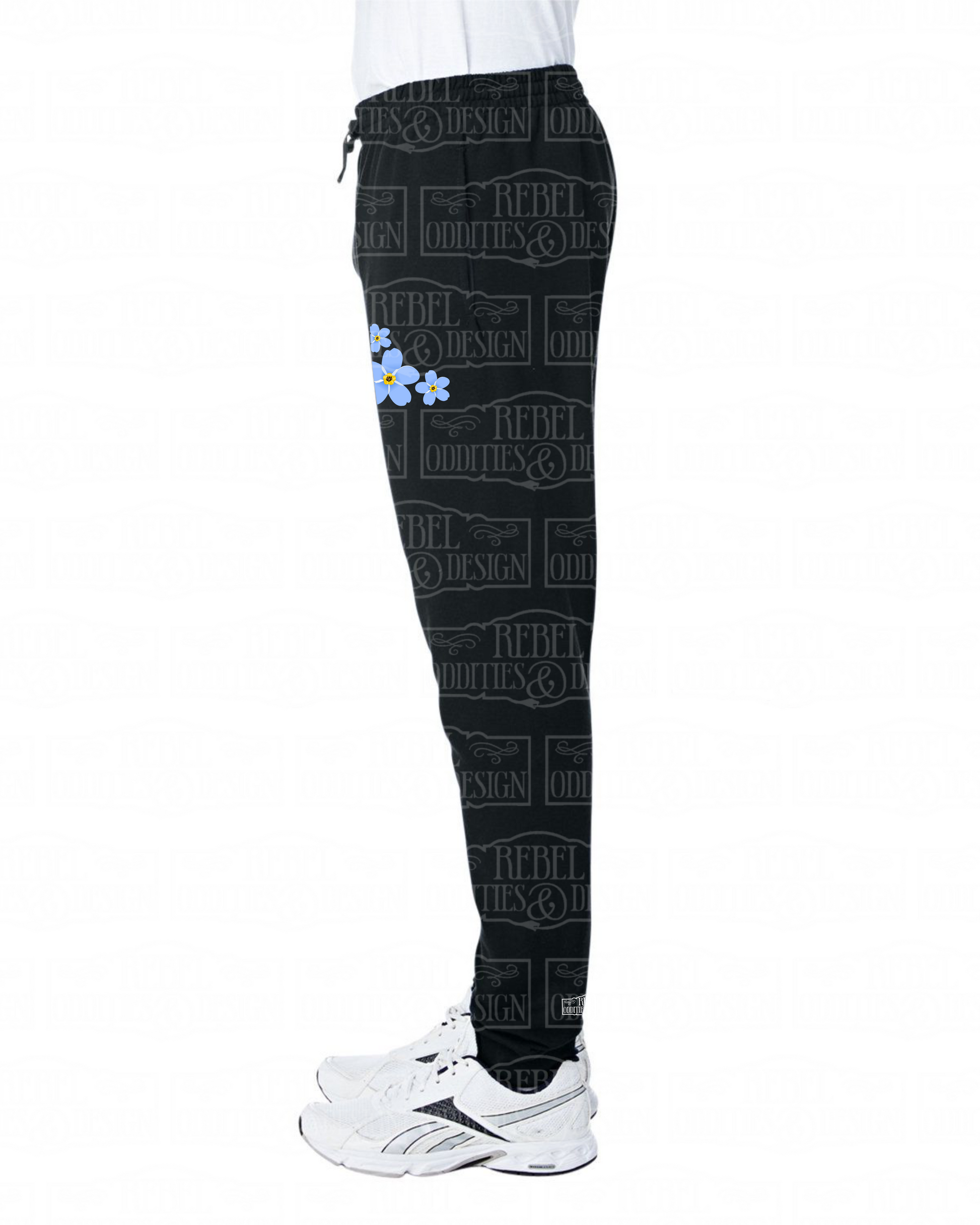 Left side view of Black jogger sweatpants with a fireweed design up the side of the right leg, featuring script reading 'Alaska' and three forget-me-nots below the left pocket, along with a small version of the logo on the back of the left leg, all on a white background.