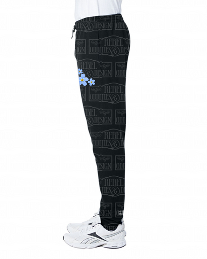Left side view of Black jogger sweatpants with a fireweed design up the side of the right leg, featuring script reading 'Alaska' and three forget-me-nots below the left pocket, along with a small version of the logo on the back of the left leg, all on a white background.